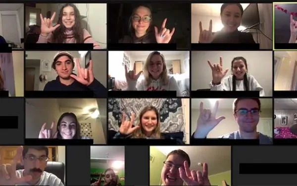 A group of people in a zoom meeting signing "I love you"